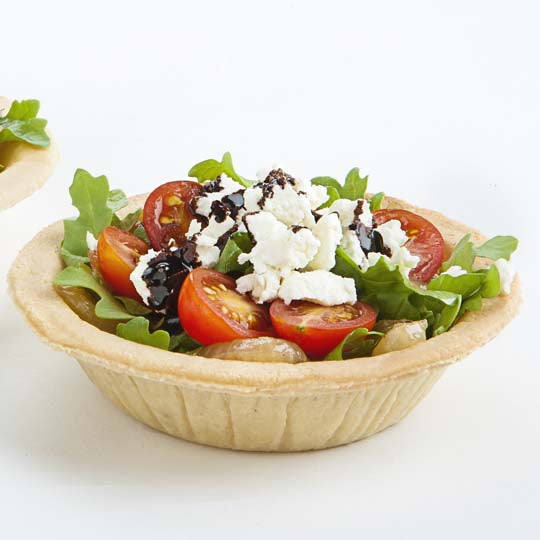 Two unsweetened almond pie shells filled with arugula, cherry tomato topped with cheese on white background