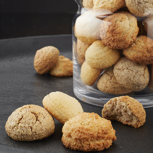 Golden italian amaretti almond macaroons scattered on black table with clear jar full of cookies to the side