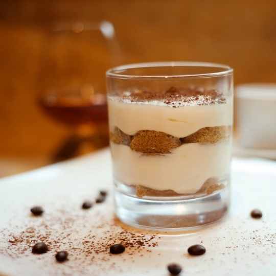 Woman holding clear jar full of tiramisu in one hand while other hand scoops the dessert with a spoon