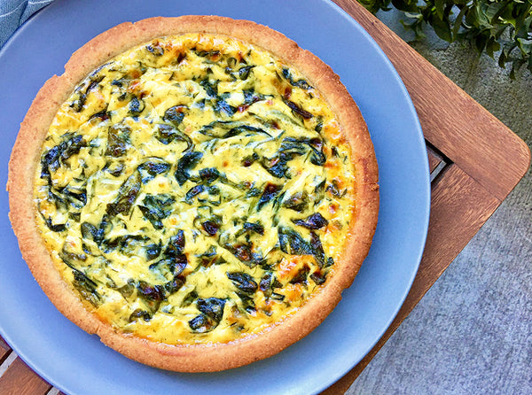 Golden spinach quiche in piccola cucina almond crust shell on blue plate resting on the edge of a brown patio table